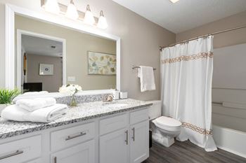 The en-suite full bathroom features granite counters, white cabinets and vanity lighting.